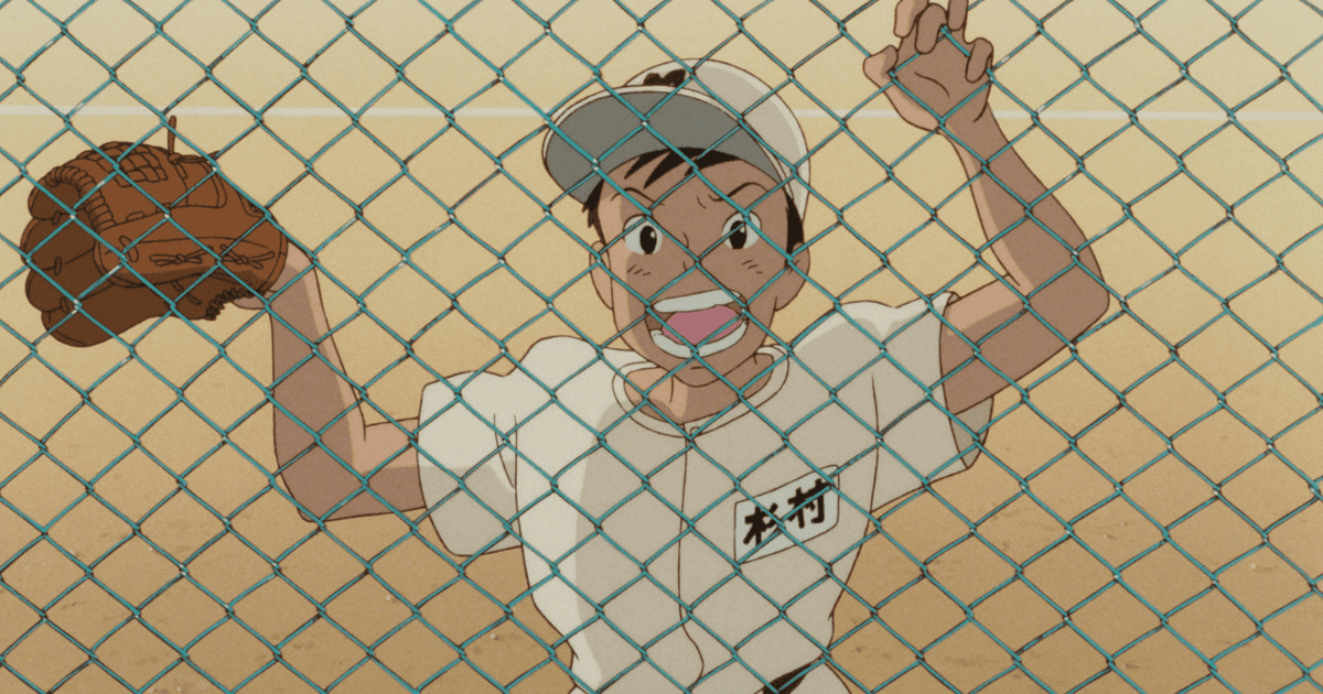 Teenage baseball player smiling behind a chain-link fence while holding a glove on a school field