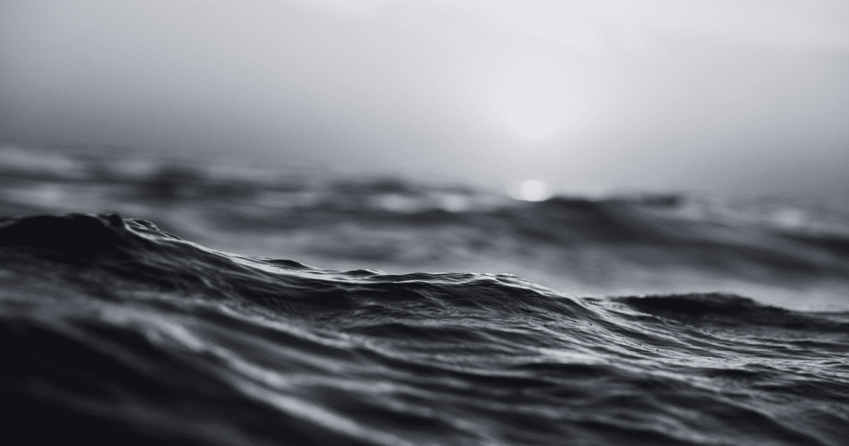 Black-and-white close-up of ocean waves beneath a hazy sun on the horizon